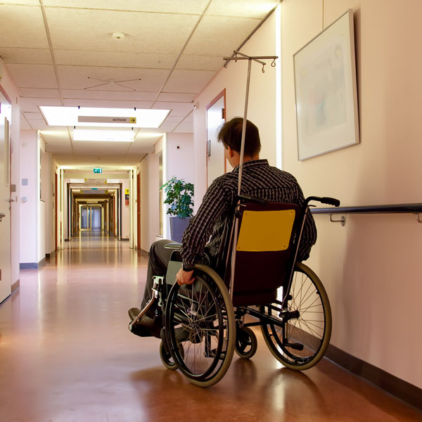 A man in wheelchair in a care facility hallway.