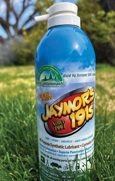 A 9.5oz aerosol can of Jaymor's all-purpose synthetic lubricant with grass and trees in the background. 