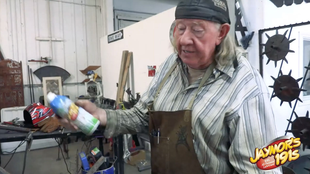 Load video: This video shows a man working in a shop using Jaymor's 191S synthetic lubricant to protect metal sculptures he makes.